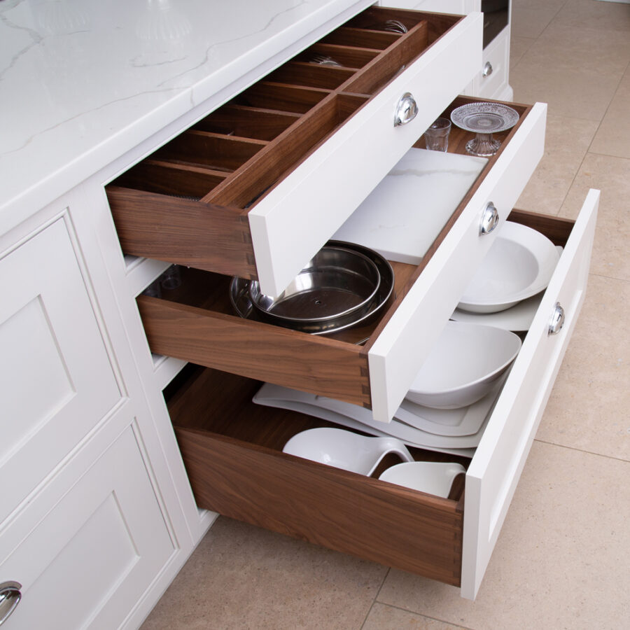 A kitchen cabinet with a Bespoke Dovetail Drawer - Classic Bespoke full of dishes and utensils.